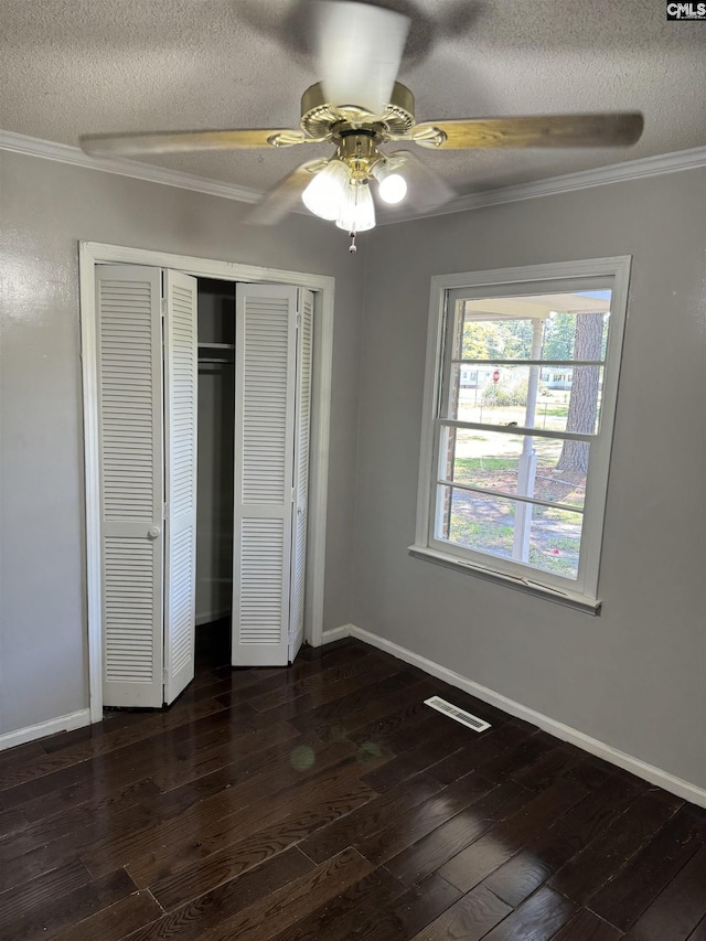 unfurnished bedroom featuring visible vents, ornamental molding, dark wood-style flooring, a textured ceiling, and a closet