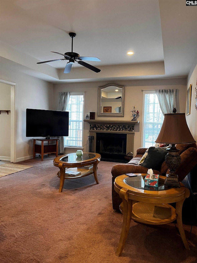 living area with carpet floors, plenty of natural light, a fireplace, and a tray ceiling