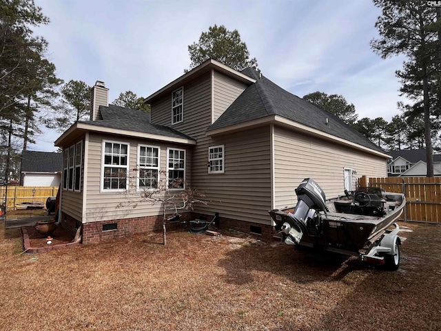 rear view of property with a shingled roof, crawl space, a chimney, and fence