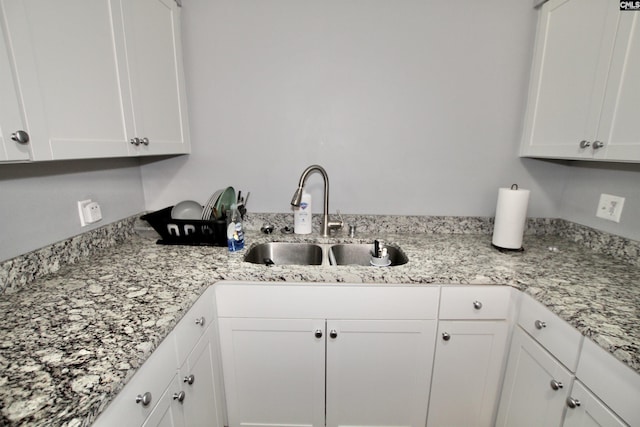 kitchen featuring light stone counters, white cabinets, and a sink