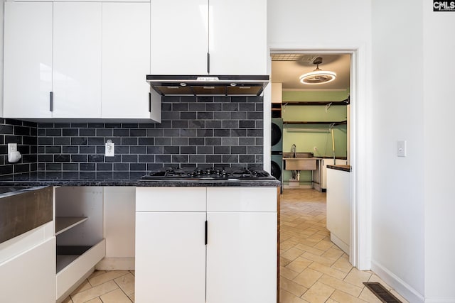 kitchen featuring under cabinet range hood, white cabinets, backsplash, and black gas stovetop