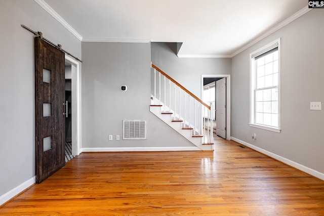 entryway featuring a barn door, light wood-style flooring, visible vents, stairs, and crown molding