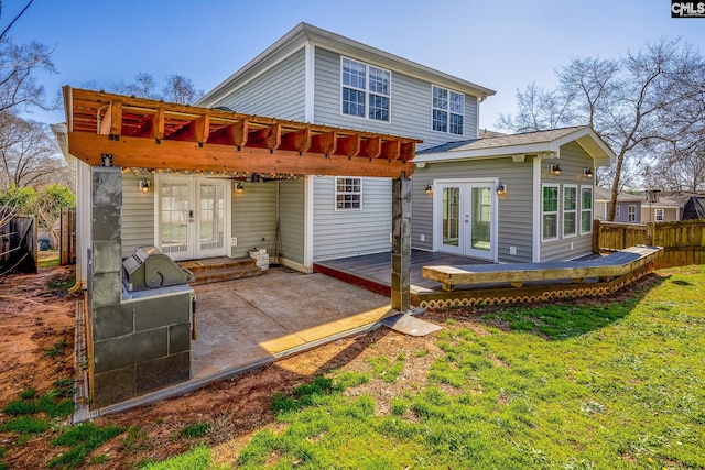 rear view of property with a deck, a patio, fence, french doors, and a lawn