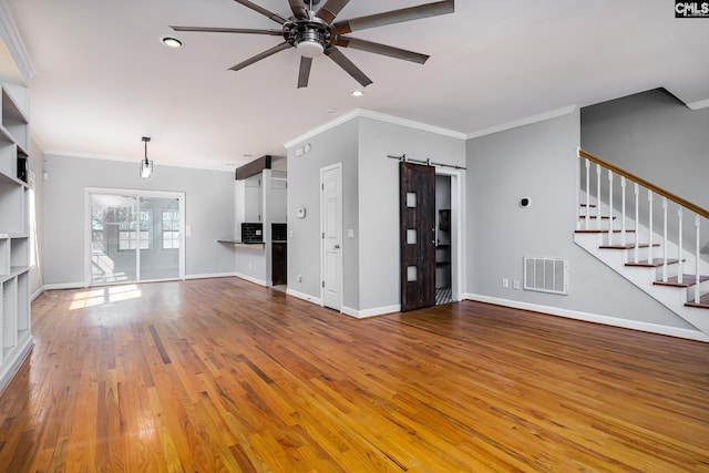 unfurnished living room with visible vents, stairway, a barn door, ceiling fan, and wood finished floors