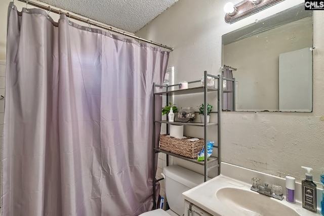 full bath with a textured ceiling, a textured wall, toilet, vanity, and a shower with curtain