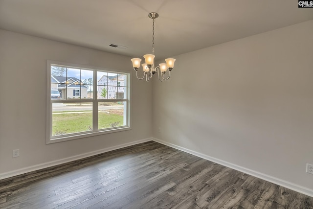 spare room with dark wood-type flooring, an inviting chandelier, visible vents, and baseboards