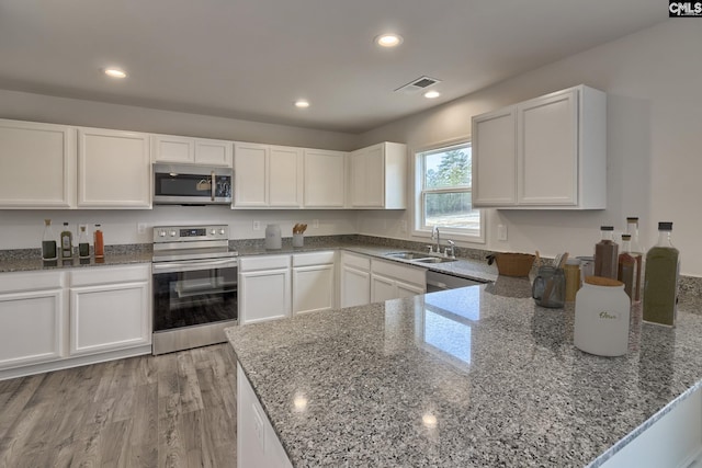 kitchen with stone countertops, white cabinetry, stainless steel appliances, and a sink