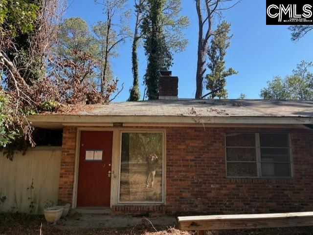 entrance to property featuring a chimney and brick siding