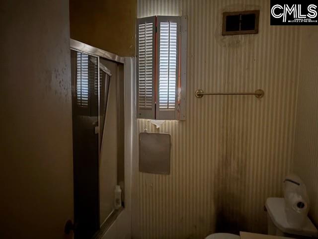 full bathroom with toilet, wallpapered walls, and combined bath / shower with glass door