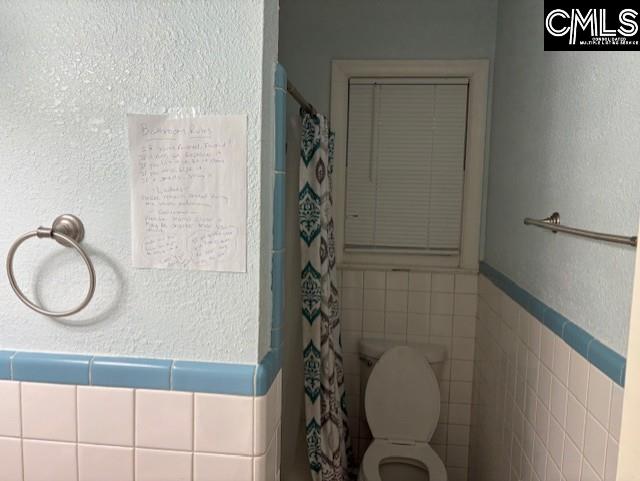 bathroom featuring toilet, a shower with shower curtain, and tile walls