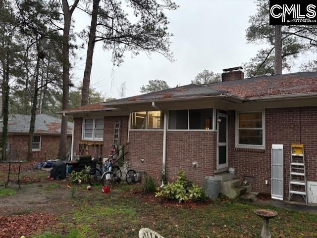 rear view of house with entry steps, brick siding, and a chimney