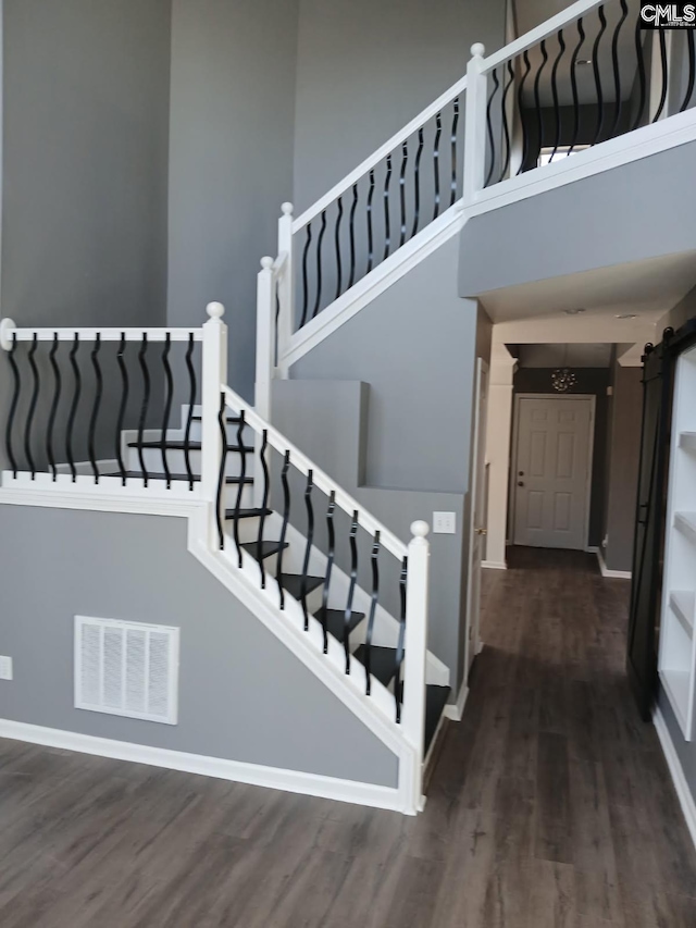 stairs featuring visible vents, a towering ceiling, a barn door, wood finished floors, and baseboards