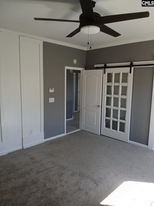 unfurnished bedroom with ornamental molding, a barn door, and carpet flooring