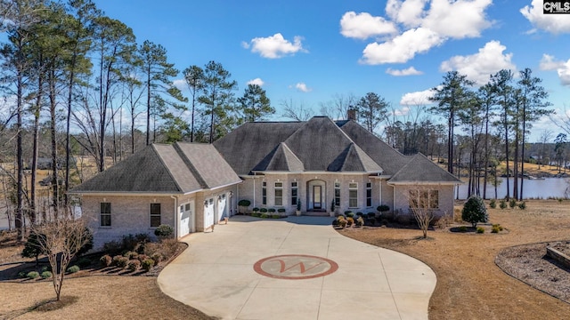 view of front of house with brick siding, a chimney, a water view, a garage, and driveway