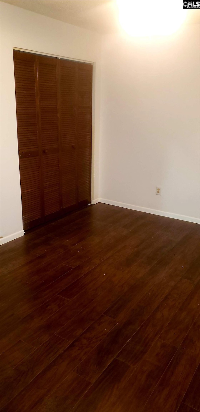 unfurnished bedroom with dark wood-type flooring, a closet, and baseboards