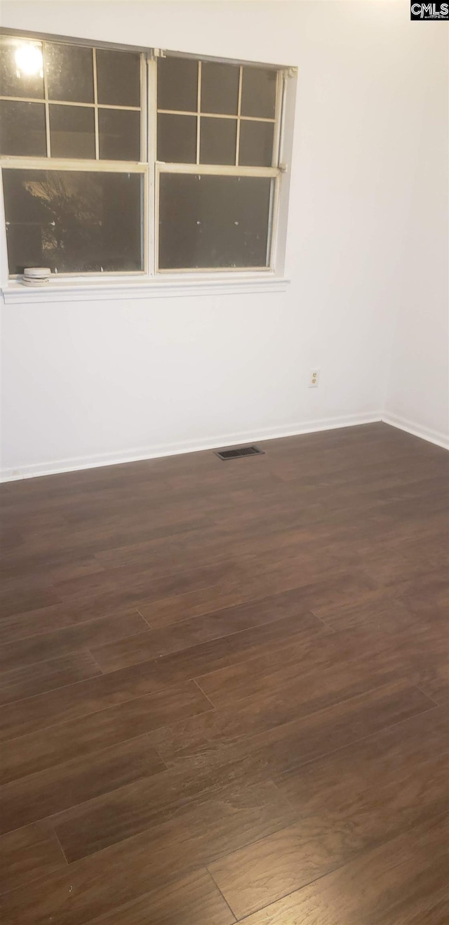 unfurnished room with dark wood-type flooring, visible vents, and baseboards