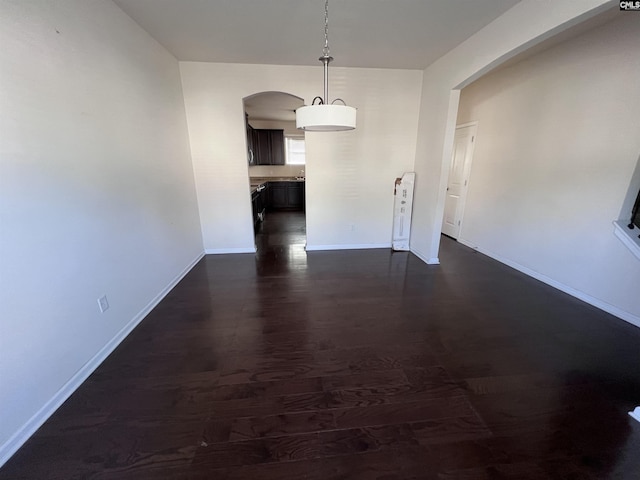 interior space with arched walkways, dark wood-style flooring, and baseboards