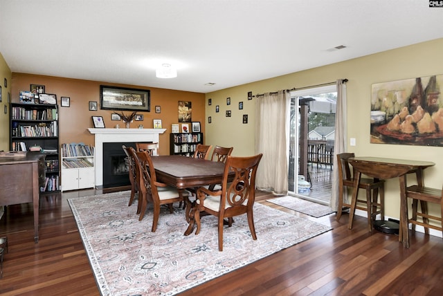 dining space featuring visible vents, dark wood-type flooring, and a glass covered fireplace