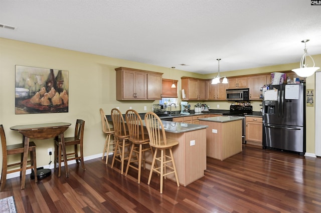 kitchen with dark countertops, appliances with stainless steel finishes, hanging light fixtures, and a center island