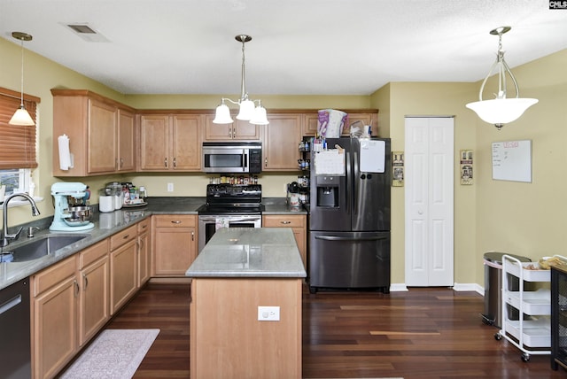 kitchen featuring dark wood-style floors, pendant lighting, appliances with stainless steel finishes, a sink, and a kitchen island