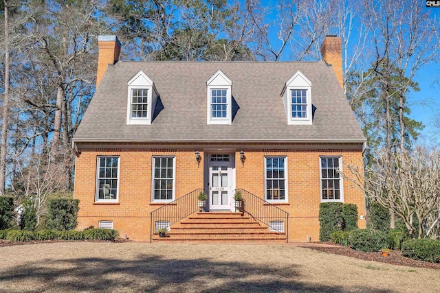 cape cod-style house with brick siding, a chimney, and a shingled roof