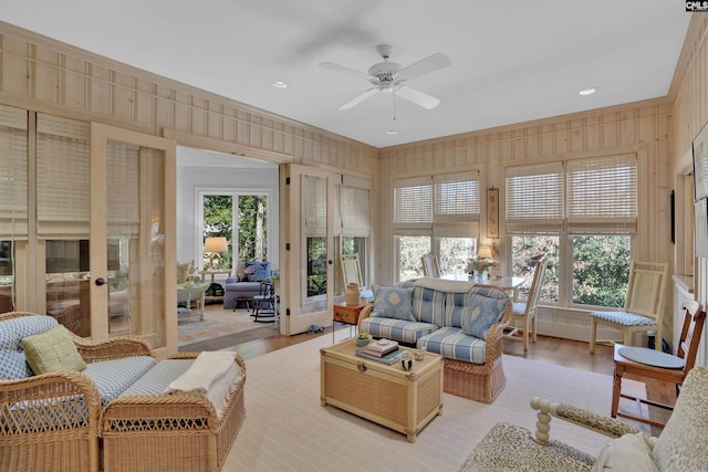 living room featuring light wood finished floors, crown molding, wooden walls, and a ceiling fan