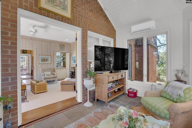 living area featuring a wealth of natural light, stone tile flooring, a wall mounted air conditioner, and vaulted ceiling