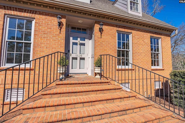 entrance to property featuring crawl space, roof with shingles, and brick siding