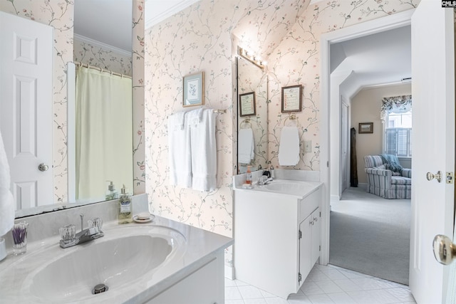 bathroom featuring crown molding, two vanities, a sink, and wallpapered walls