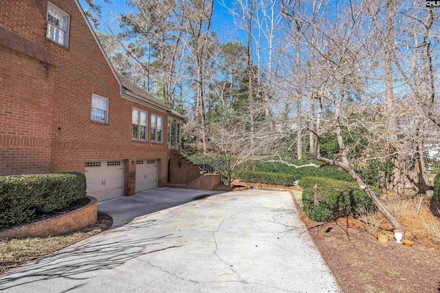 view of side of property featuring a garage, concrete driveway, and brick siding