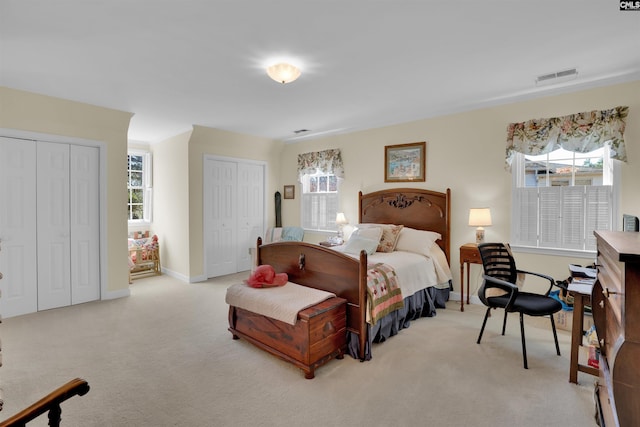 bedroom with multiple closets, light colored carpet, visible vents, and baseboards