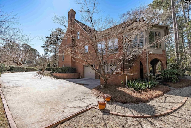 exterior space with a garage, brick siding, driveway, and a chimney