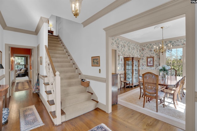 dining area with ornamental molding, wood finished floors, a notable chandelier, and wallpapered walls