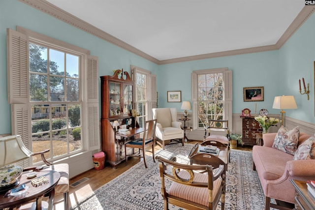 living area featuring a healthy amount of sunlight, a wainscoted wall, light wood-style flooring, and visible vents