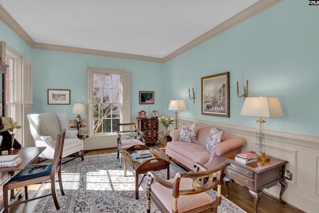 living area with ornamental molding, wood finished floors, and wainscoting