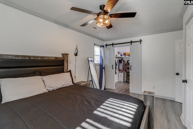 307 Wyoming Dr, Sumter, SC 29153 - bedroom with a barn door, dark wood-style floors, a walk in closet, crown molding, and a textured ceiling