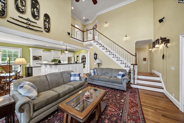 living area with a towering ceiling, stairway, dark wood-style flooring, and ornamental molding