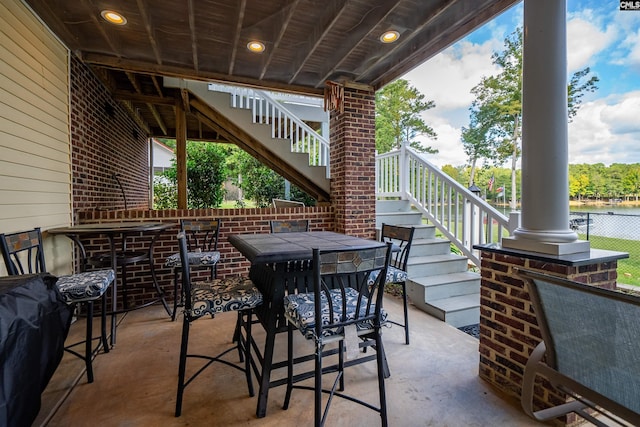 view of patio / terrace featuring outdoor dining area, a water view, fence, and stairway