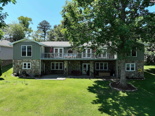 rear view of house with stone siding, a patio area, a lawn, and french doors