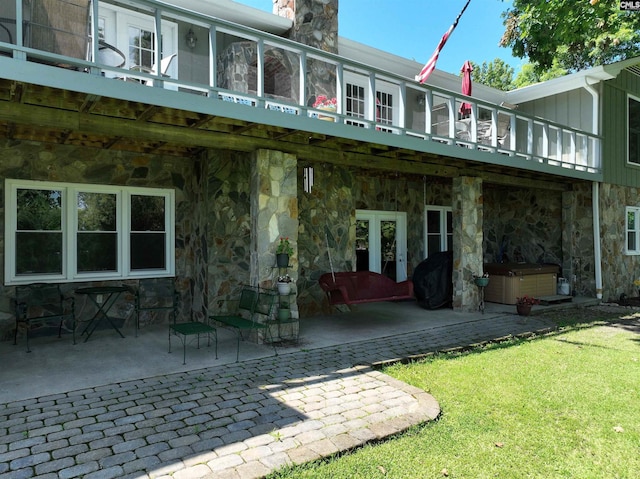 back of house featuring a chimney, stone siding, a patio area, and a hot tub