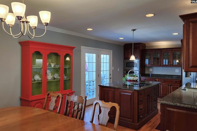 kitchen featuring stainless steel appliances, dark stone countertops, decorative light fixtures, and an island with sink