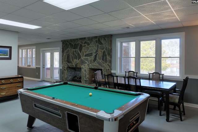 rec room with french doors, a drop ceiling, and a stone fireplace