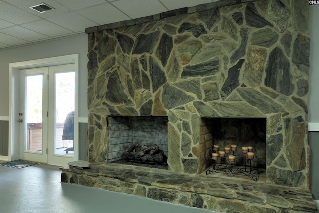 room details featuring visible vents, a drop ceiling, and a stone fireplace