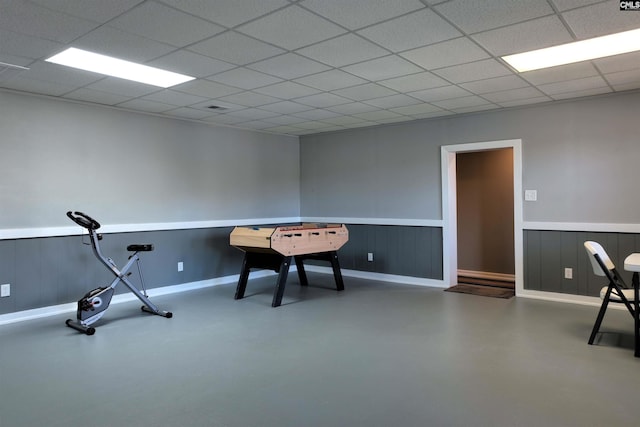 game room with finished concrete flooring, a wainscoted wall, a paneled ceiling, and baseboards