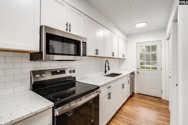 kitchen with light stone counters, appliances with stainless steel finishes, white cabinets, and a sink