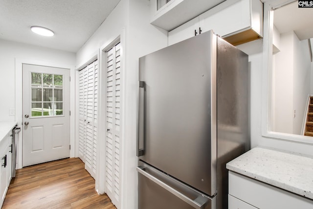 kitchen featuring light wood finished floors, white cabinets, light stone counters, freestanding refrigerator, and a textured ceiling