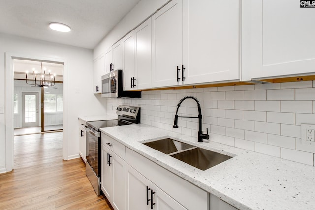 kitchen featuring appliances with stainless steel finishes, a sink, light stone countertops, and white cabinets