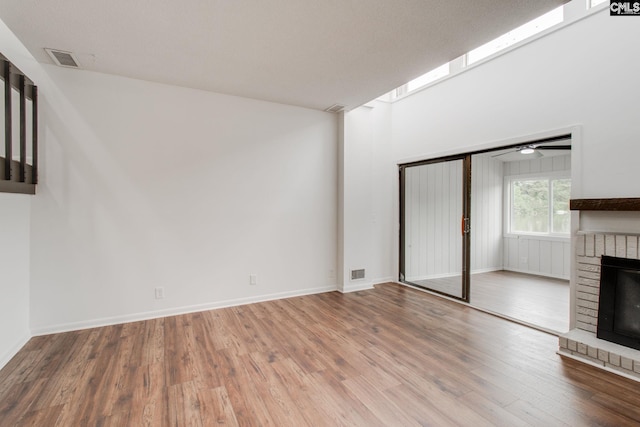 unfurnished living room featuring a brick fireplace, visible vents, baseboards, and wood finished floors