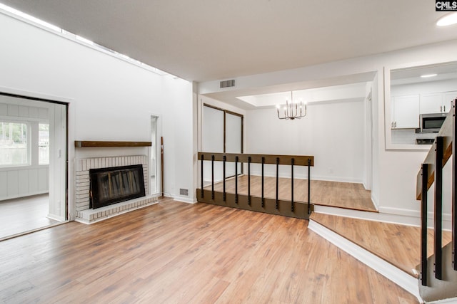 unfurnished living room with visible vents, baseboards, a brick fireplace, light wood finished floors, and an inviting chandelier