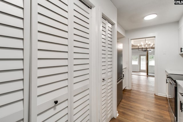 corridor with dark wood-style floors, a notable chandelier, and baseboards